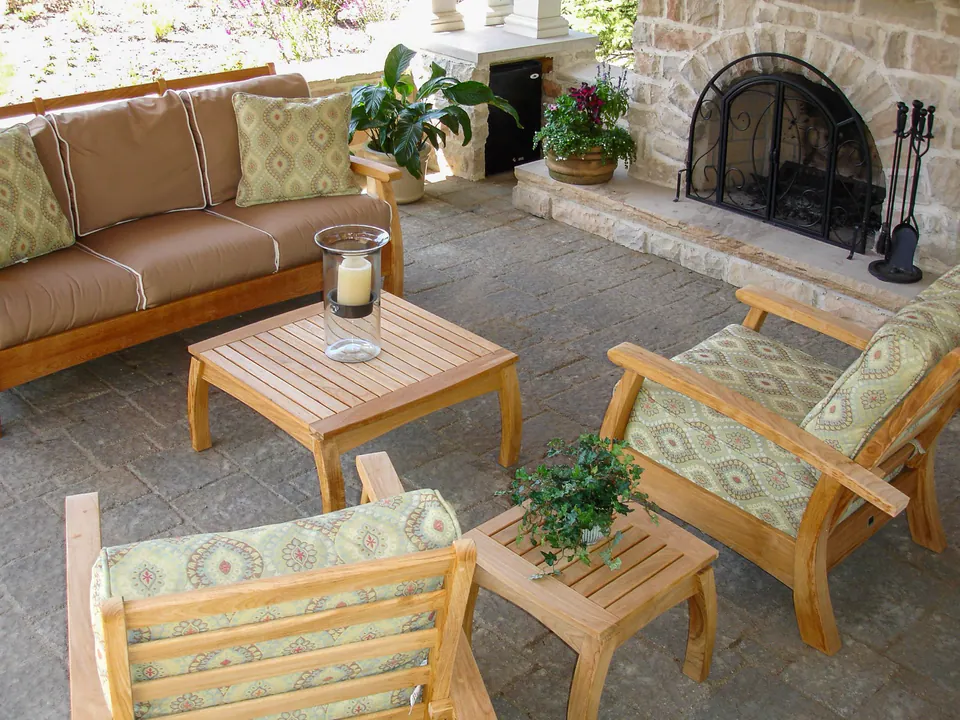 Outdoor lounge furniture arranged around a stone fireplace on a paver floor beneath a covered pavilion.